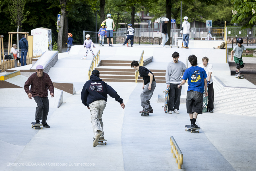 Plusieurs skaters en train de rouler sur le skatepark : on voit des modules en escalier, des pentes en béton lisse, une rampe de slide.