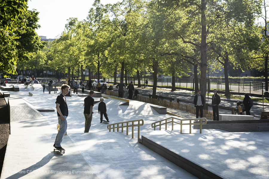 Vision d'ensemble du skatepark : des modules en escalier, des pentes en béton lisse, une rampe de slide. On voit la rue de Boston qui longe l'équipement et les assises installées le long